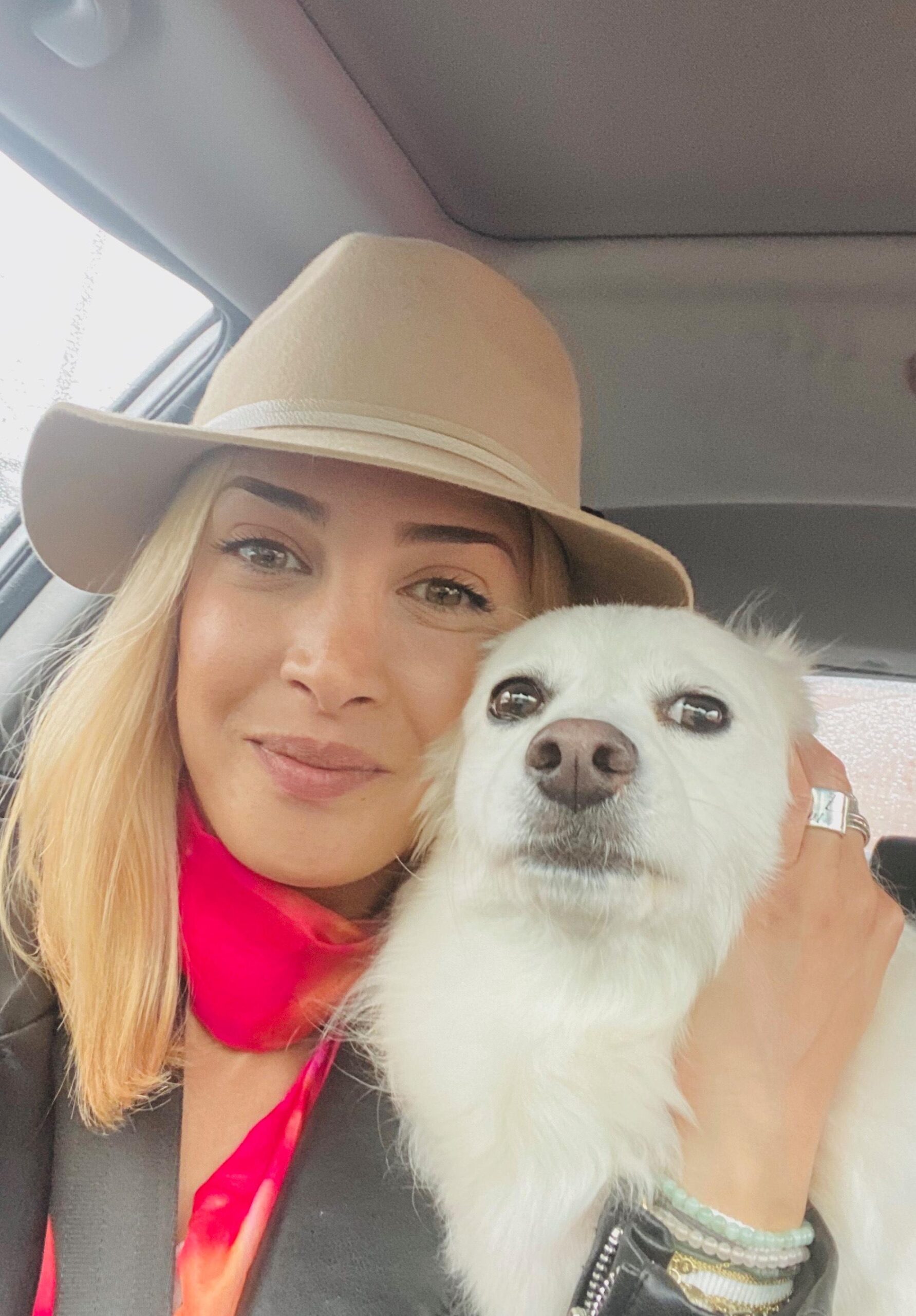 Woman wearing hat hugging white dog in car